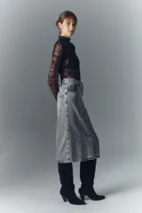Falda midi de denim rígido, color gris claro lavado, con botones metálicos grabados en el frente y recortes verticales.