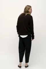 Pantalón tobillero negro de tiro medio con cintura elástica en la espalda, bolsillos delanteros y bolsillos de parche con solapa en la parte trasera. Bajo acabado con pinzas. Cierre frontal con cremallera y botón.