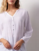 Blusa blanca de manga larga con cuello a la base y escote en V con botones. Terminación de manga con elástico.