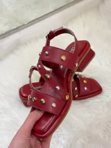 Sandalias rojas de cuero con tiras cruzadas y detalle de tachas plateadas y doradas.