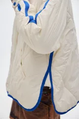 Campera acolchada color crema con cierre frontal y cuello alto. Presenta dos franjas azules en las mangas y ribete azul en el cuello y ruedo.