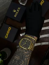 Reloj Casio Quartz dorado con caja cuadrada, dial negro y pulsera de eslabones.