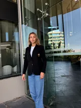 Blazer negro de algodón con solapas de muesca, cierre con un botón dorado, bolsillos de parche y aplique bordado en el pecho.