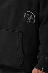 Buzo canguro negro de frisa rústica con corte oversize y capucha. Presenta un pequeño logo blanco en el pecho y un bolsillo tipo canguro.