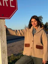 Campera color beige de tejido de punto en lana con detalles en cuero marrón en los bolsillos. Corte recto con cuello amplio y cierre con botones. Talle 1.