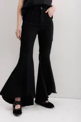 Pantalón de jean negro elastizado con corte ajustado y volados en la parte baja de la pierna. El ruedo es más largo en la parte trasera y tiene terminación descosida.