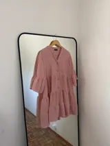 Vestido corto de silueta amplia, confeccionado en polina melange, con escote en V, botones al frente y recortes con volados. Las mangas son 3/4 con leve volumen.
