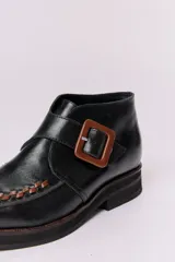 Botín acordonado de cuero marrón con textura grabada y hebilla lateral. Tiene suela de goma negra y puntera redondeada con costuras decorativas.
