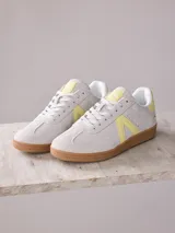 Championes de mujer color gris claro con detalles en amarillo y suela marrón.