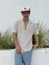 Camisa tejida a rayas verticales color beige y blanco, de corte recto, manga corta y cuello cubano.