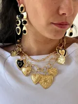 Collar dorado con doble cadena, una de eslabones grandes y otra de eslabones pequeños, con múltiples dijes de corazones dorados y negros.