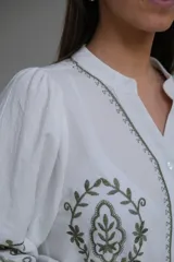 Camisa blanca de manga larga con elástico en puños, cuello mao con botones en la parte delantera y bordados florales en verde.