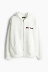 Campera blanca con capucha y cierre frontal, con bolsillos tipo canguro y puños acanalados. Estampado frontal con el logo de Dua Lipa y la frase "Training Season".