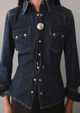 Camisa de denim azul oscuro con cuello camisero, cierre frontal con botones a presión, dos bolsillos con solapa abotonada en el pecho y mangas largas con puños abotonados. Incluye bolo tie con dije plateado y turquesa.