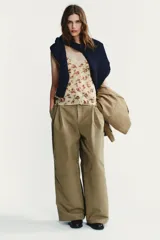 Pantalón color beige de tiro medio con trabillas, bolsillos laterales, de plastrón en pierna y detalle de solapas en espalda. Detalle de pinzas en delantero y cierre frontal con cremallera y ganchos metálicos.