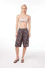 Bermuda unisex de poliéster con estampado de camuflaje y banda lateral color crema con texto en cursiva.