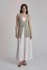 Chaleco largo de tejido de punto color verde salvia, sin mangas, con escote en V pronunciado y cierre frontal con cordón ajustable a la altura del busto.