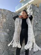 Ruana larga de lana merino color beige jaspeado, con diseño de trenzas y flecos en el borde inferior.