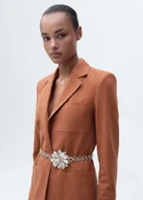 Blazer color ladrillo con solapas de muesca, cierre frontal con botón, bolsillo de parche en el pecho y dos bolsillos de parche frontales. Incluye cinturón plateado con forma de flor.