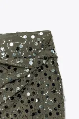 Falda pantalón verde militar con lentejuelas plateadas y negras, de tiro alto, con delantero cruzado y nudo.