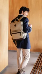 Mochila beige de tela canvas combinada con detalles en símil cuero marrón. Tiene apertura superior con cierre, bolsillo frontal con cierre, bolsillos laterales, bolsillos internos, asa corta de mano y correas acolchonadas regulables para la espalda.