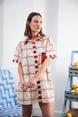 Vestido camisero corto con estampado a cuadros en tonos beige, rojo y azul. Tiene cuello camisero, botones frontales, bolsillo en el pecho y corte recto.
