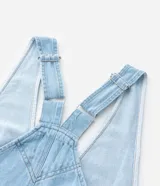 Mono peto de jeans celeste confeccionado en algodón certificado BCI. Tiene breteles anchos ajustables, bolsillos delanteros y traseros, y bajo largo.