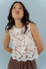 Blusa blanca de encaje con cuello redondo a la base y sin mangas.