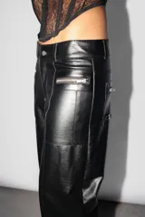 Pantalón recto de cuerina color negro, tiro medio-bajo con recortes en el delantero. Acceso mediante cartera de cierre metálico. Cintura con presillas y botón zamak personalizado Top White. Todos sus bolsillos con cierres metálicos. Dos tiras decorativas con botón snap en piernas delanteras. Detalle de avío pasador marcario en trasero.