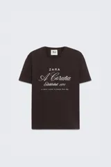 Camiseta marrón de algodón con cuello redondo y mangas cortas. Estampado frontal con el texto "Zara A Coruña Established 1975 A Rúa Juan Flórez 64-66" en color blanco.