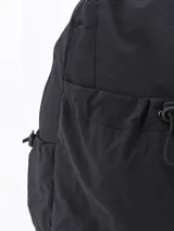 Mochila de tela color crema con bolsillo frontal con cordón ajustable, bolsillos laterales y correas de tela.