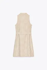 Vestido corto color beige con bordados florales perforados, cuello solapa, sin mangas, cinturón de tela con hebilla redonda y cierre frontal con botones.