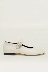 Zapato estilo Mary Jane color blanco hueso, de cuero vacuno, con punta redondeada, tira sobre el empeine con hebilla plateada y suela de cuero.