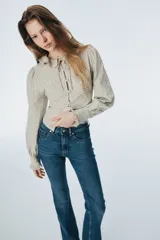 Jean de denim azul con tiro alto, cierre con botón y piernas amplias con bajos acampanados.