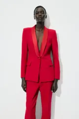 Blazer roja de corte recto, con cuello smoking de satén negro, mangas largas con hombreras, bolsillos frontales con solapa y cierre frontal con un botón.