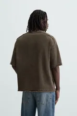 Camiseta marrón de corte holgado, cuello redondo y manga corta. Tiene un efecto lavado y terminaciones irregulares.