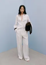 Camisa blanca de lino con cierre de botones, bolsillo de parche en el pecho, manga larga con puños abotonados, diseño recto y cuello camisero.