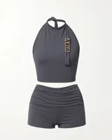 Conjunto deportivo gris compuesto por un top halter con logo dorado y shorts ajustados con fruncido lateral.