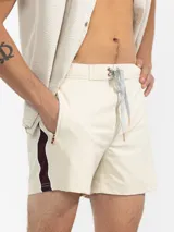 Short de baño color beige con una franja vertical marrón en el lateral. Tiene cintura elástica con cordón ajustable, bolsillos laterales y trasero con cierre, y suspensor de malla fina hipoalergénica.