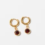 Par de aros dorados tipo argolla con dije colgante de piedra facetada color rojo oscuro.