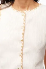 Top blanco de poliéster y elastano, con cuello redondo, sin mangas y cierre frontal con botones.