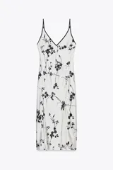 Vestido largo blanco con estampado de flores negras, escote pico y tirantes finos con ribete negro.