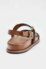 Sandalias planas color marrón con doble tira delantera con detalle de hebilla y cierre mediante hebilla en la pulsera al tobillo.