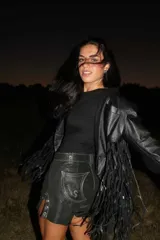 Chaqueta de cuero negra con solapas, cierre frontal con broche y flecos en mangas y ruedo.