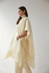 Ruana color crema de lana fina con flecos en el ruedo y bolsillos delanteros.