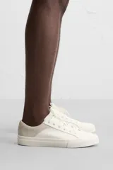 Zapatillas deportivas blancas con detalle de color a contraste en el talón y suela con acabado irregular.