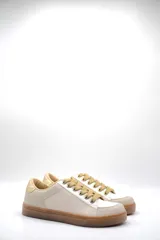 Zapatillas bajas color marfil con detalles dorados en el talón y ojales metálicos. Suela de goma color caramelo y cordones beige.