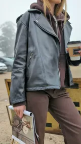Chaqueta de cuero ovino color marrón, con cuello clásico, cierre asimétrico con cremallera, solapas con botones a presión, múltiples bolsillos con cremallera y cinturón ajustable en la cintura.