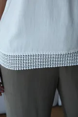 Musculosa blanca de corte holgado, sin mangas, con cuello redondo y un bolsillo pequeño en el pecho. El ruedo inferior presenta un detalle de encaje o puntilla calada.