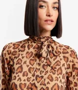 Vestido largo de chiffon con estampa de corazones con diseño de leopardo. Tiene cuello alto con lazo, mangas largas ligeramente transparentes y falda con volado. El tejido contiene hilo metalizado.